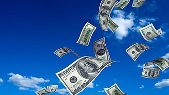 Hundred dollar bills flying in the wind against a blue sky