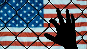 Hand holding a fence with American flag in the background