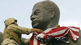 Former Cpl. Edward Chin places the U.S. Flag over a statue of Saddam signifing the liberation of the Iraqi people in 2003 during Operation Iraqi Freedom.