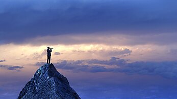 Businessman Standing Looking Through Spyglass On Mountain Peak