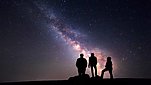 Silhouette of three people looking upwards at the Milky Way glowing brightly in the night sky