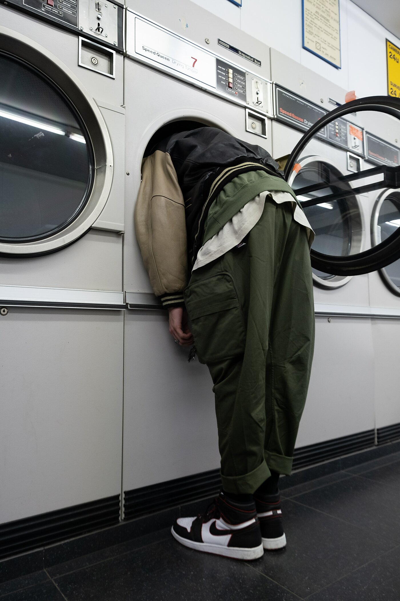 Male figure in jogging wear with their head stuck in a drum of a laundromat machine, arms hanging loose by his side