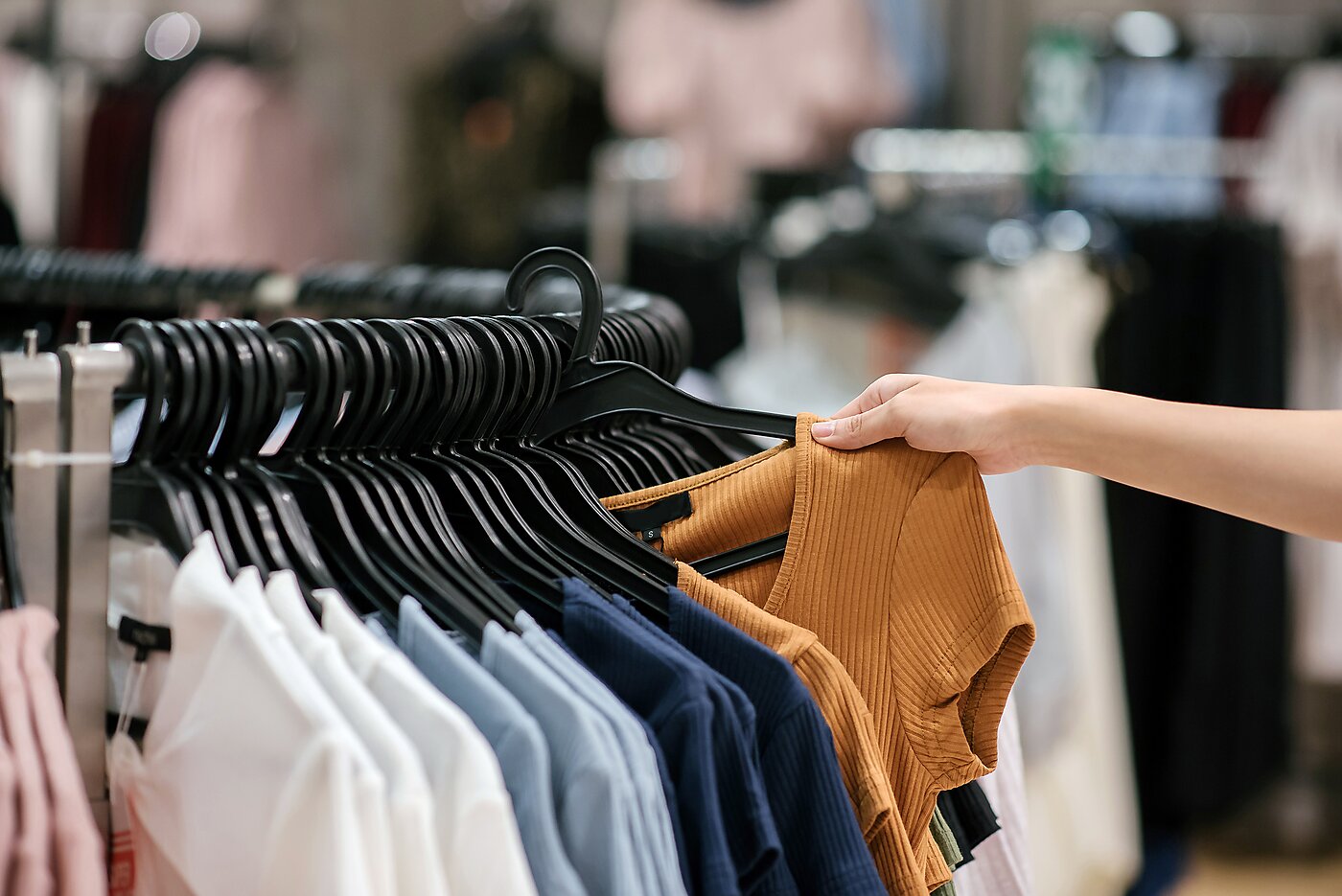 Woman's hand browsing through rack of clothes for sale